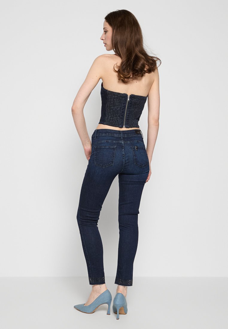Top senza spalline in denim blu con tessuto testurizzato e zip sul retro, abbinato a jeans skinny scuri e décolleté azzurro chiaro.