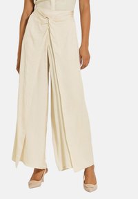 Wijde broek in een zachte, lichte crèmekleurige stof met een geknoopte detail in de taille. Glad textuur en vloeiend ontwerp, gecombineerd met nude hakken.