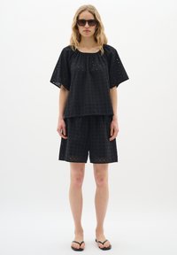 Completo in cotone nero composto da una maglietta ampia con maniche corte e un paio di pantaloni corti abbinati, entrambi con piccoli motivi intagliati.