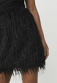 Black mini skirt made of textured, fringed material with metallic accents. The hemline is uneven, adding a layered appearance.
