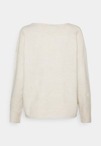 Beżowy sweter z luźnym fasonem, szerokim dekoltem, opadającymi ramionami i ściągaczami przy mankietach. Miękka, teksturowana tkanina bez wzorów i dodatków.