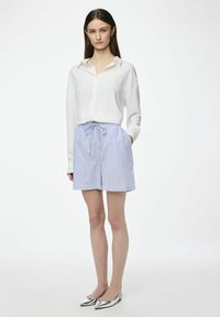Chemise blanche à manches longues avec un coupe décontractée, associée à un short à cordon de serrage rayé bleu clair et blanc. Ballerines argentées à bout pointu.