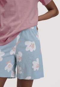 Helles rosa kurzärmliges Hemd kombiniert mit hellblauen Shorts mit weißen Blumenmustern und pfirsichfarbenen Akzenten. Aus Baumwolle, lässige Passform.