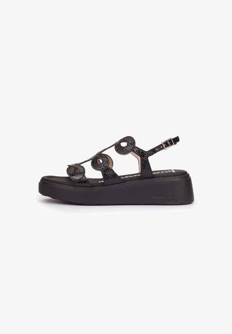 Black wedge sandal with textured circular cutout straps and adjustable ankle buckle on a thick sole.