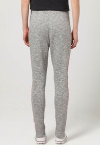 Graue Stretch-Leggings mit glatter Textur, ausgestattet mit pinken Seitenstreifen, einem figurschmeichelnden Design und einem elastischen Bund, kombiniert mit weißen Sneakers.