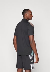 Must mustreheline mustikaelusega, millel on roosad triibud õlgadel, koos mustade lühikeste pükstega, millel on valged ja mustad vertikaalsed triibud ning Adidas'i logo.