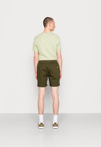 Olijfgroene shorts met een elastische tailleband, zijzakken en een achterzak, gecombineerd met een lichtgroene T-shirt met korte mouwen.