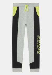 Grijze sweatpants met zwarte zijpanelen, neon groene accenten, een elastische tailleband en een grafische print met de tekst "OPGERICHT IN 1981."