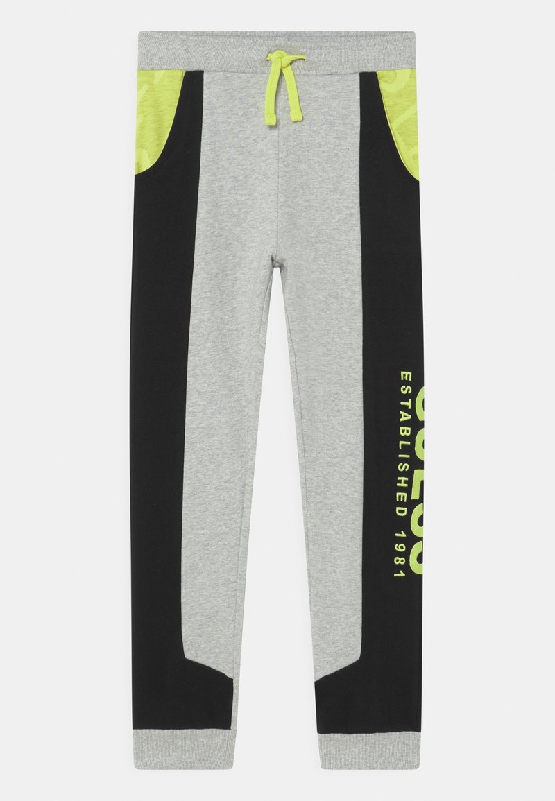 Grijze sweatpants met zwarte zijpanelen, neon groene accenten, een elastische tailleband en een grafische print met de tekst "OPGERICHT IN 1981."
