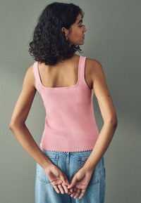 Różowy dopasowany top na ramiączkach z kwadratowym dekoltem, prążkowaną fakturą i falbaniastym wykończeniem, połączony z high-waist niebieskimi dżinsami.