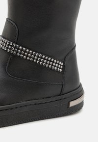 Melna sintētiska kurpju zābaku ar rhinestones joslu, teksturētu virsmu, noapaļotu formu un plakanu gumijas zoli ar akcenta detaļu.