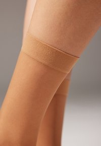 Beige hojt strømper med en glat tekstur og elastisk bånd, der har en mat finish og en tætsiddende design for sikker pasform.