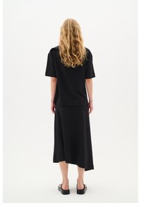 Čierny dvojdielny outfit pozostávajúci z krátkotričkového topu a midi sukne. Tkanina vyzerá hladko, s uvoľneným strihom a asymetrickým lemom.