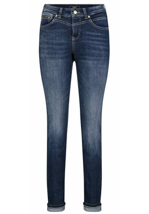 Jean skinny bleu foncé avec ourlets roulés, fermeture avant par bouton et zip, avec des décolorations visibles sur les cuisses et les genoux.