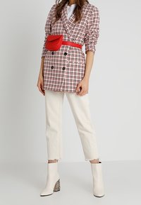 Kaksirivinen ruudullinen bleiseri vaaleanpunaisena ja valkoisena, yhdistettynä kermaisiin farkkuihin. Varustettu punaisella vyölaukulla ja valkoisilla nilkkureilla, joissa on teksturoitu korko.