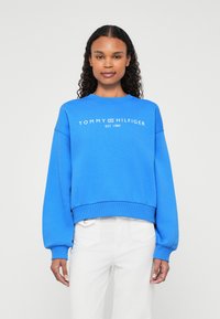 Modrá mikina vyrobená z bavlny, s okrúhlym výstrihom, dlhými rukávmi a rebrovaným spodným okrajom. Zobrazuje logo "TOMMY HILFIGER EST. 1985".