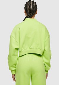 Felpa a maniche lunghe in cotone verde neon brillante, con spalle scese e orlo a costine, abbinata a pantaloni della tuta coordinati.