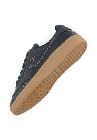 Baskets noires avec une tige en cuir lisse, des lacets en coton texturé, des clous métalliques et une semelle en caoutchouc marron avec un motif ondulé.