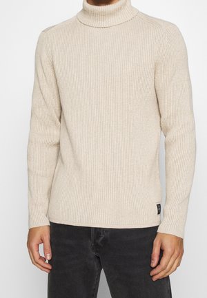 Beige gerippter Rollkragenpullover mit langen Ärmeln und einer taillierten Passform. Verfügt über ein kleines schwarzes Logo-Tag unten links.