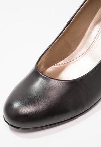 Chaussure ballerine plate en cuir noir avec bout arrondi et doublure intérieure rembourrée beige sur fond blanc.