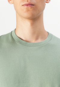 Tricou cu mânecă scurtă și guler rotund din țesătură verde deschis. Textură netedă, cu o croială obișnuită, având cusături discrete la guler.