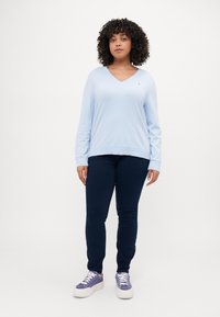 Lyseblå langermet V-hals skjorte med ribbestrikket kant, kombinert med mørk marineblå skinny bukser og lilla sneakers med hvite såler.