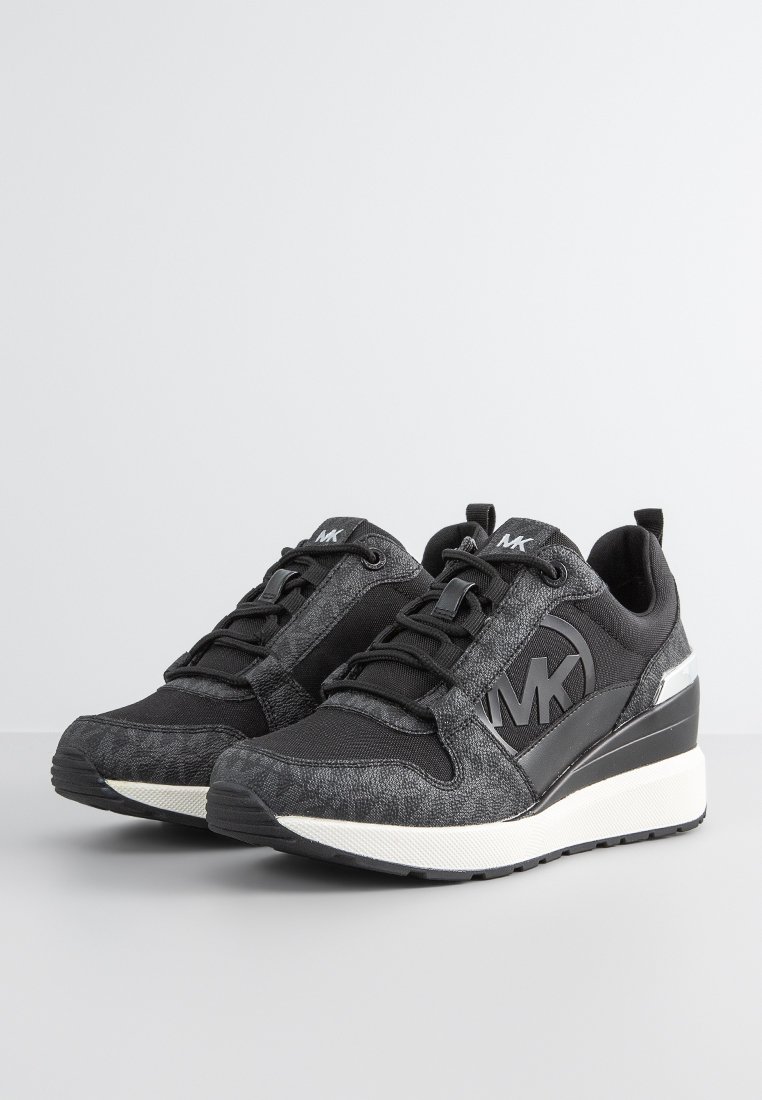 Zwarte sportieve schoenen met gestructureerde stof, gestroomlijnd ontwerp, vetersluiting aan de voorkant en een verhoogde zool. Beschikt over een prominente logo en reflecterende accenten.