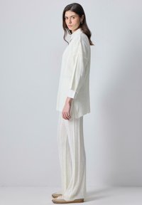 Top de punto blanco con cuello tipo polo, combinado con pantalones de pierna ancha a juego. Ambos presentan un patrón texturizado y un ribete acanalado.