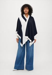 Námorníkově modrý a bílý šátek s geometrickým vzorem, hladká tkanina, volný střih, spárováno s širokými denimovými kalhotami, reflexní stříbrné boty.