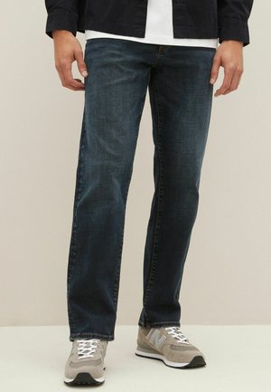 Dark blue denim jeans with a straight leg design, featuring a slightly textured finish and standard five-pocket styling. Worn with gray sneakers.