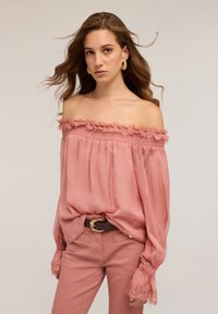 Blusa rosa trasparente off-the-shoulder con bordo arricciato e polsini arricciati, abbinata a pantaloni rosa e una cintura marrone con fibbia dorata.