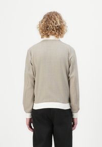 Lys grå bomberjakke med en tekstureret finish, elastiske ærmer og hvidt taljebånd. Enkel, minimalistisk design uden synlige mønstre.