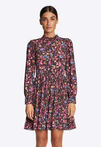 Černé šaty s dlouhými rukávy, zdobené barevným leopardím potiskem v růžové, modré a béžové barvě. Plisovaná sukně dodává texturu a pohyb.