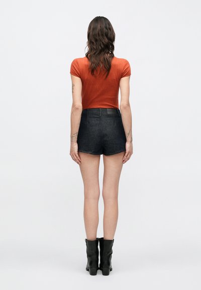 Μαύρα τζιν σορτς με ψηλή μέση, σε συνδυασμό με εφαρμοστή μπλούζα σε σκουριά χρώμα, από πίσω. Μαύρα μποτάκια αστραγάλου ολοκληρώνουν το ντύσιμο.