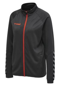 Veste de sport noire avec un motif texturé, dotée d'une fermeture éclair rouge et d'accents, de poignets élastiques et de bandes en chevron blanches sur les manches.