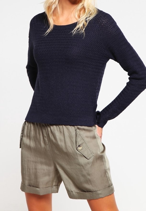Femme portant un pull à manches longues bleu marine texturé et un short ample olive clair avec des poches avant à boutons.