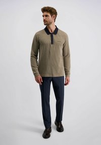 Beige Langarm-Polohemd mit strukturiertem Muster, marineblauer Kragen und dreiknöpfiger Knopfleiste, kombiniert mit dunkelblauen Hosen und schwarzen Schuhen.
