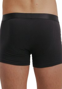 Uomo che indossa slip neri attillati, vista posteriore che mostra l'elastico e la parte superiore delle gambe.