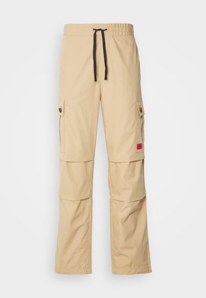 Pantaloni cargo beige con vita elastica, coulisse nera, tasche laterali e un piccolo logo rosso sulla coscia.