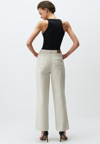 Breedpijp crèmekleurige denim broeken met een textuurafwerking, met twee achterzakken en een klein leren label. Gecombineerd met een zwarte tanktop en hakken.