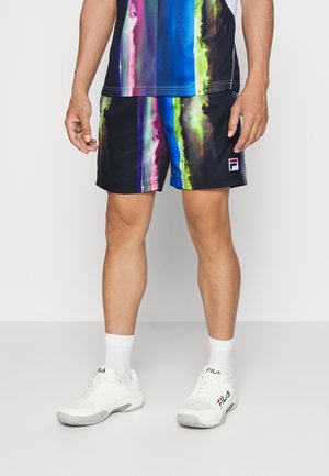 Mand iført sorte shorts med lodrette farverige striber, hvide sokker og hvide FILA-sneakers, stående mod en ensfarvet baggrund.