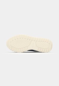 Shoe sole view, featuring textured cream rubber with a herringbone pattern and a clean, smooth edge for grip and stability.