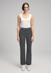 Wit geribbeld tanktop gecombineerd met zwarte broek met een wit stippenpatroon, aangevuld met witte sneakers.