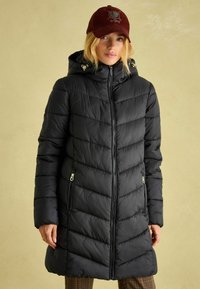 Melnā pūkainā jaka ar kapuci, ar ševronu kviltējuma rakstu, priekšējā rāvējslēdzēja aizdari un sānu rāvējslēdzēja kabatām. Akcentēta ar zelta detaļām.