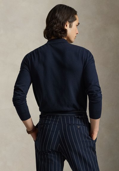 Navy blue knit polo shirt with a soft texture, featuring long sleeves and a relaxed fit, paired with pinstriped trousers.