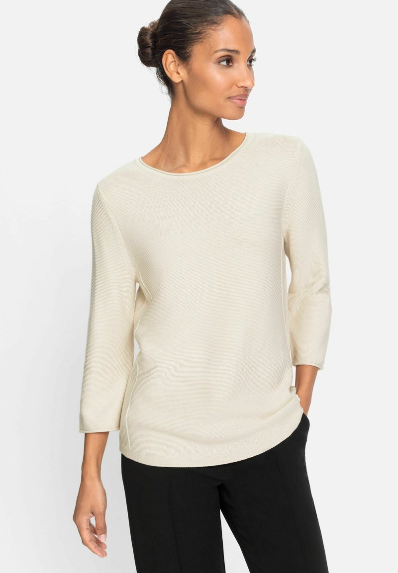 Strickpullover in Creme mit rundem Halsausschnitt, dreiviertelärmeln und lässiger Passform, kombiniert mit schwarzen Hosen. Glatte Textur.