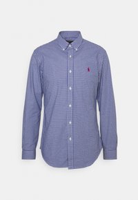 Modrá a bílá kostkovaná košile s dlouhým rukávem a límcem na knoflíčky, s malým červeným logem na hrudi a zakřiveným zakončením.