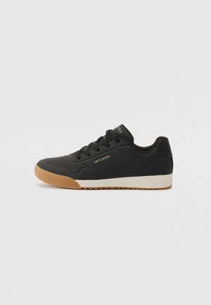 Zapatillas negras con superficie sintética lisa, diseño de cordones, acentos perforados y suela de goma. Presenta el logotipo "SKECHERS" en dorado.