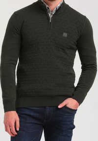 Pull-over vert foncé avec col à demi-zip, présentant un motif en diamant texturé et des poignets et ourlets côtelés.