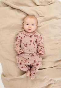 Világosrózsaszín, virágmintás ruházat fodros gallérral és mandzsettával, bézs színű, texturált szövet alapon rétegezve. Baba fekve.